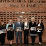 Distinguished Educators lined up in from of hall of fame wall