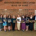 Distinguished Educators inductees lined up in front of the hall of fame wall, holding their plaques.